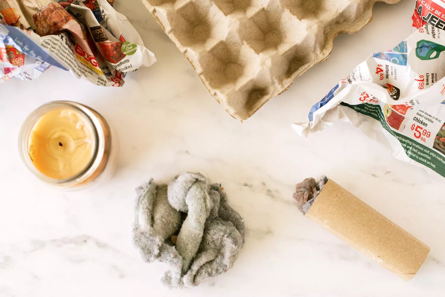 Xơ vải máy sấy được vo tròn bên cạnh cuộn giấy vệ sinh đầy xơ vải, báo nhàu nát và nến